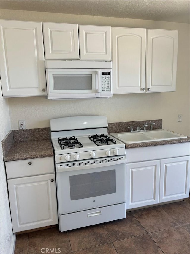 6688 Yucca Ave Unit 29, Palms, CA 92277 - kitchen with white appliances, white cabinetry, dark countertops, a sink, and dark tile patterned floors