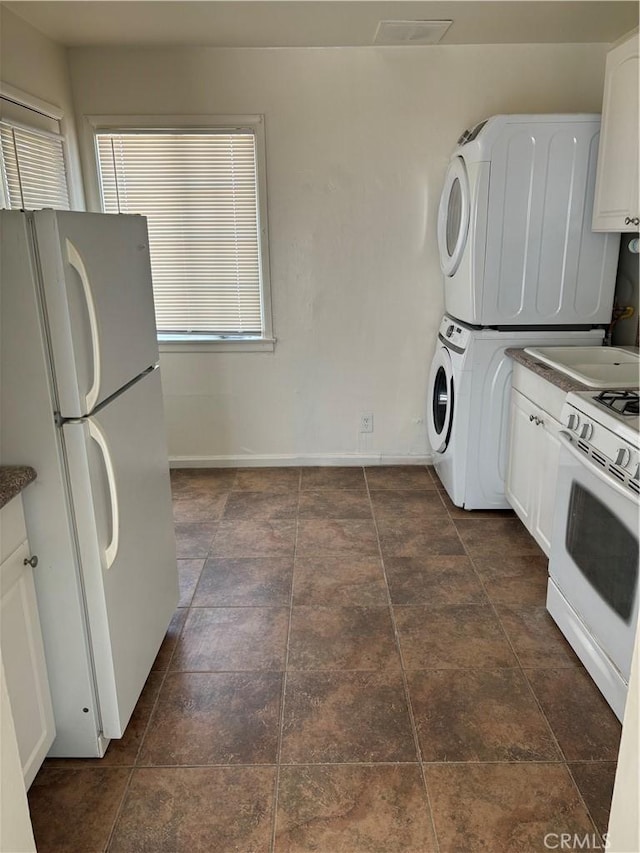 6688 Yucca Ave Unit 29, Palms, CA 92277 - kitchen with white appliances, stacked washer / dryer, dark countertops, and white cabinetry