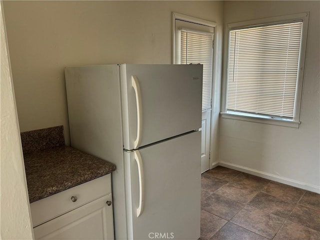 6688 Yucca Ave Unit 29, Palms, CA 92277 - kitchen featuring freestanding refrigerator, dark countertops, baseboards, white cabinets, and dark stone finish flooring