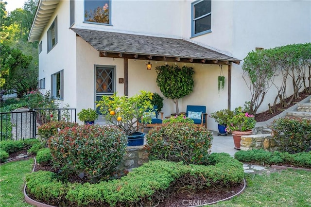 doorway to property featuring stucco siding and a shingled roof