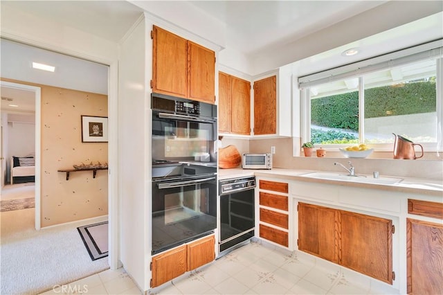 kitchen featuring black appliances, light countertops, brown cabinetry, and a sink