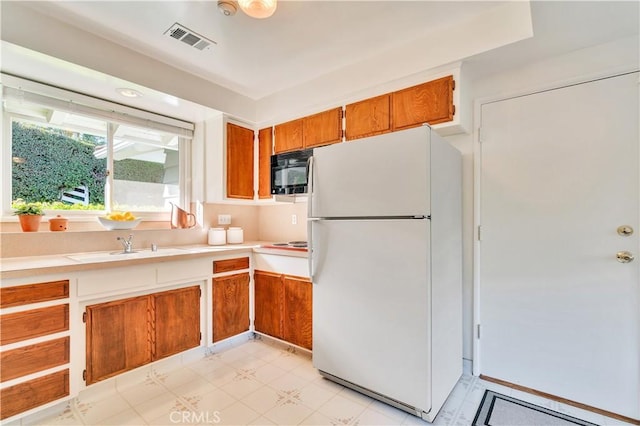 kitchen with freestanding refrigerator, black microwave, light countertops, and brown cabinets