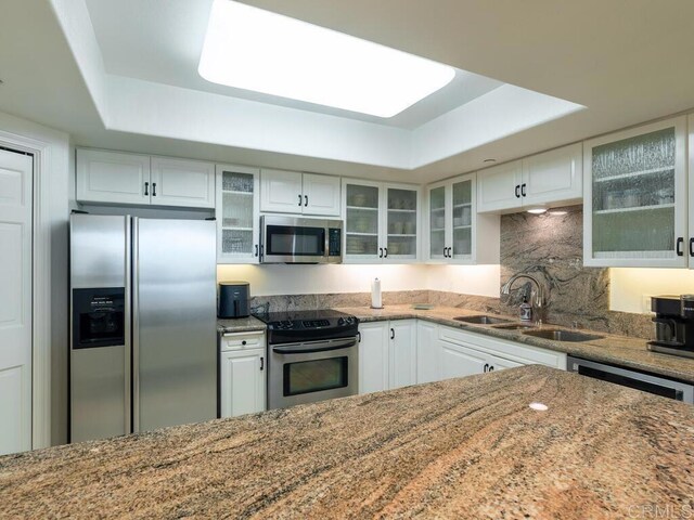 1099 1st St Unit 217, Coronado, CA 92118 - kitchen featuring appliances with stainless steel finishes, a raised ceiling, white cabinetry, and light stone counters