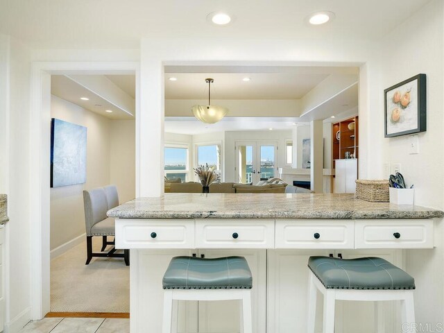 1099 1st St Unit 217, Coronado, CA 92118 - kitchen featuring light stone countertops, white cabinetry, light colored carpet, open floor plan, and decorative light fixtures