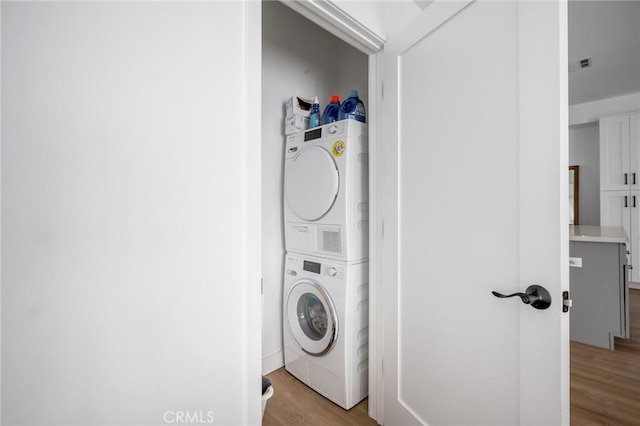 washroom with stacked washer and clothes dryer and light wood-type flooring