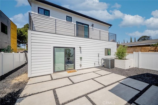 rear view of property featuring a balcony, central AC unit, a fenced backyard, and a patio area
