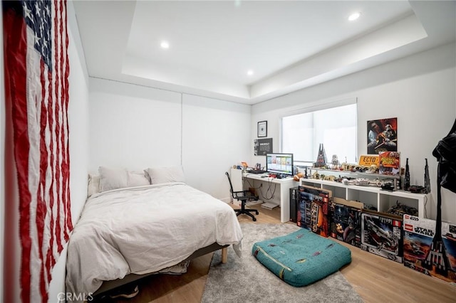 bedroom with a tray ceiling, wood finished floors, and recessed lighting