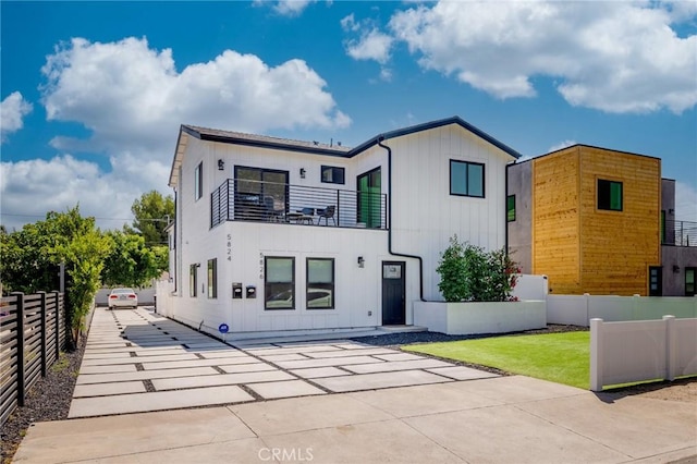 view of front of property featuring a balcony, concrete driveway, board and batten siding, fence, and a patio area