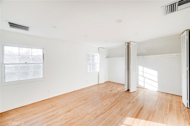 unfurnished bedroom featuring multiple windows, light wood finished floors, and two closets
