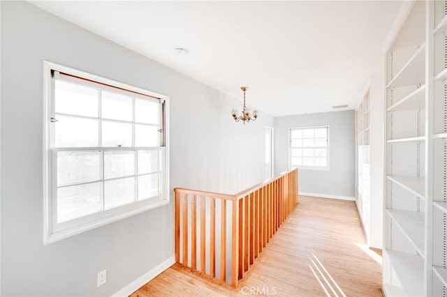 hall featuring a chandelier, light wood-style floors, and baseboards
