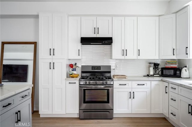 kitchen featuring stainless steel gas range, under cabinet range hood, black microwave, decorative backsplash, and light wood-style flooring