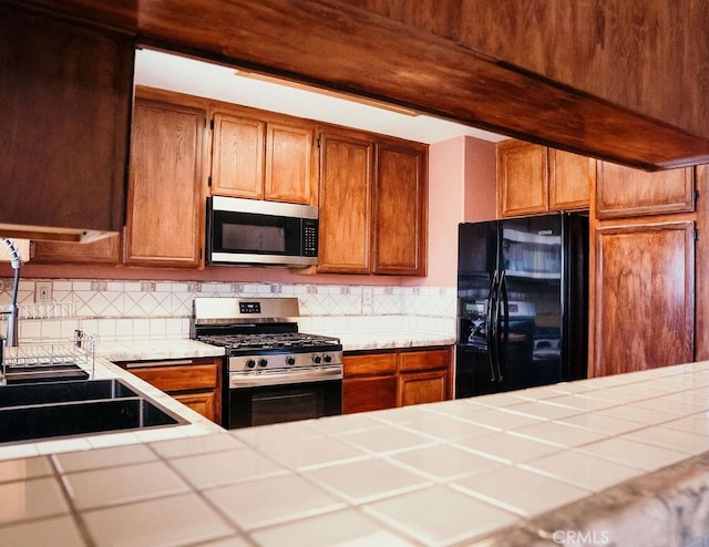 25657 Tamarisk St, Barstow, CA 92311 - kitchen featuring stainless steel appliances, tile countertops, a sink, tasteful backsplash, and brown cabinetry