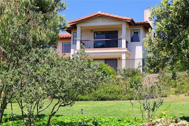 view of front of house featuring a balcony, a tile roof, stucco siding, and a front lawn