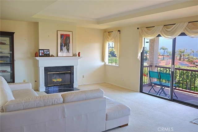 living room with carpet, a glass covered fireplace, a raised ceiling, crown molding, and baseboards