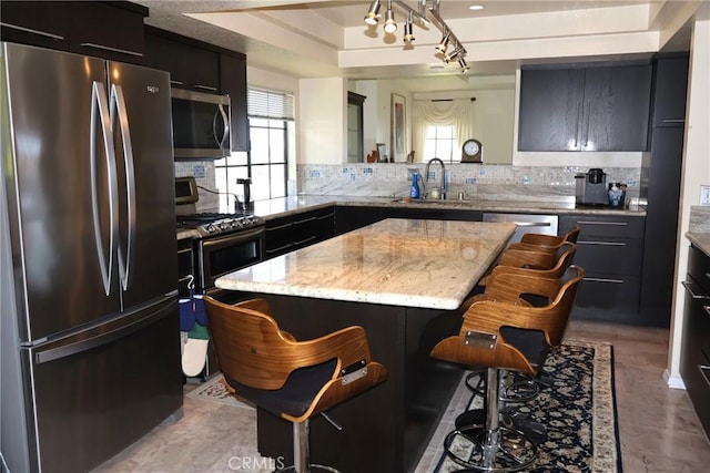 kitchen with appliances with stainless steel finishes, a sink, a tray ceiling, a breakfast bar, and backsplash