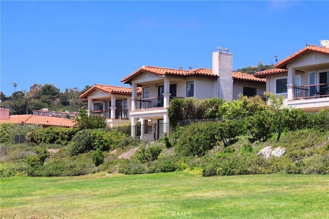 back of house featuring a chimney, a tile roof, stucco siding, and a lawn