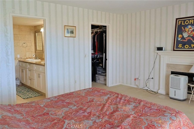 bedroom with a sink, wallpapered walls, a walk in closet, connected bathroom, and a closet