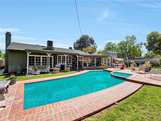 view of pool with outdoor lounge area, a patio area, fence, a pool with connected hot tub, and a storage shed