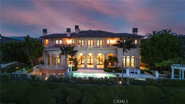 12 Skyridge, Newport Coast, CA 92657 - back of property at dusk with a chimney, a patio, a balcony, and stone siding