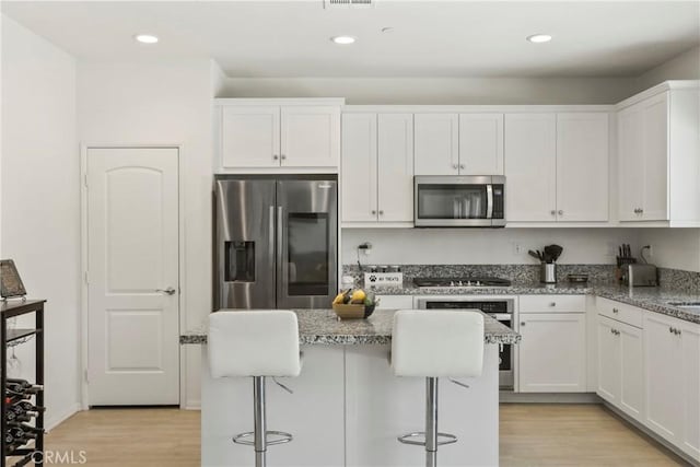30527 Expedition Dr, Winchester, CA 92596 - kitchen with stainless steel appliances, white cabinets, light stone counters, light wood-style flooring, and a breakfast bar