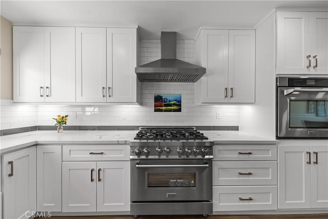 kitchen with stainless steel appliances, wall chimney range hood, white cabinetry, and light stone counters