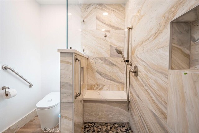 bathroom featuring tiled shower, toilet, and baseboards