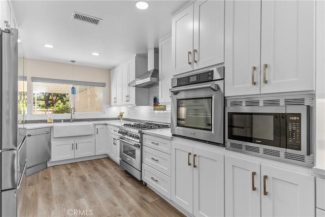 kitchen with stainless steel appliances, wall chimney range hood, a sink, white cabinetry, and light countertops