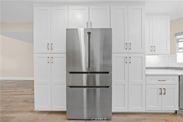 kitchen featuring freestanding refrigerator, light wood finished floors, light countertops, baseboards, and white cabinetry