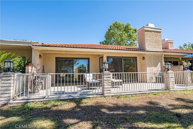 view of front of house featuring stucco siding, a chimney, a patio area, and fence
