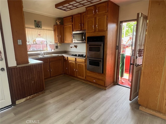 kitchen with stainless steel appliances, brown cabinetry, light wood finished floors, and a sink