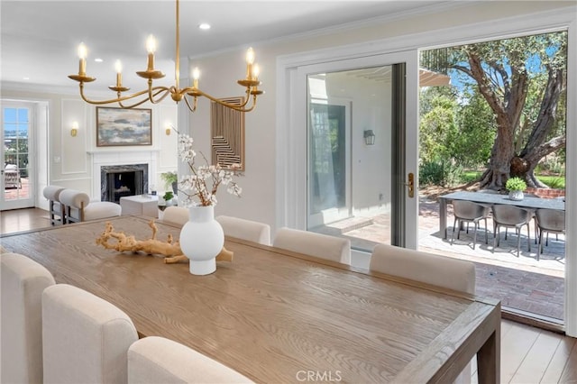 dining area with crown molding, a chandelier, light wood-type flooring, and a fireplace