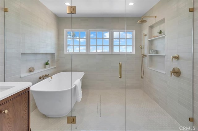 bathroom featuring a stall shower, a freestanding bath, vanity, tile walls, and recessed lighting