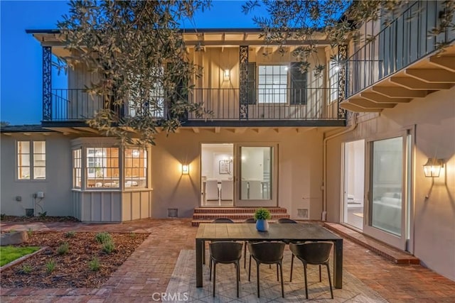 back of house with a balcony, stucco siding, a patio area, and outdoor dining space