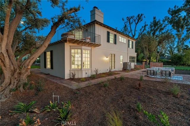 view of home's exterior featuring a balcony, an outdoor hangout area, a chimney, a patio, and fence