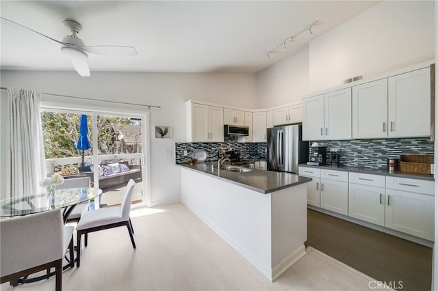 kitchen with appliances with stainless steel finishes, dark countertops, vaulted ceiling, tasteful backsplash, and light wood finished floors