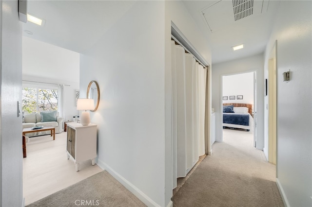 corridor with attic access, light colored carpet, and baseboards