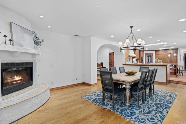 dining room with recessed lighting, arched walkways, light wood-style flooring, a chandelier, and a lit fireplace