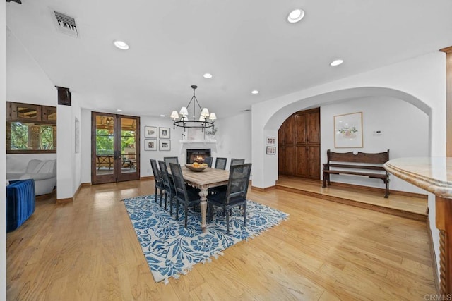 dining room featuring french doors, arched walkways, recessed lighting, a warm lit fireplace, and light wood-style floors