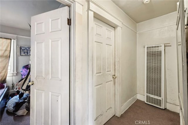 hallway with a heating unit and dark colored carpet
