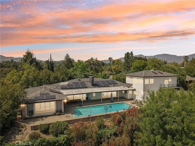 12218 Sarazen Pl, Granada Hills, CA 91344 - back of property at dusk with roof mounted solar panels, a patio area, an outdoor pool, and a mountain view