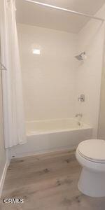 full bathroom with shower / bath combo with shower curtain, toilet, and wood finished floors