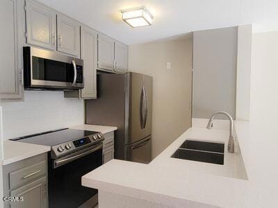 kitchen featuring stainless steel appliances, a sink, light countertops, a peninsula, and gray cabinets