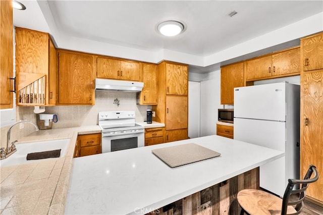 7599 Joshua Ln, Yucca Valley, CA 92284 - kitchen with white appliances, a sink, under cabinet range hood, light countertops, and brown cabinetry