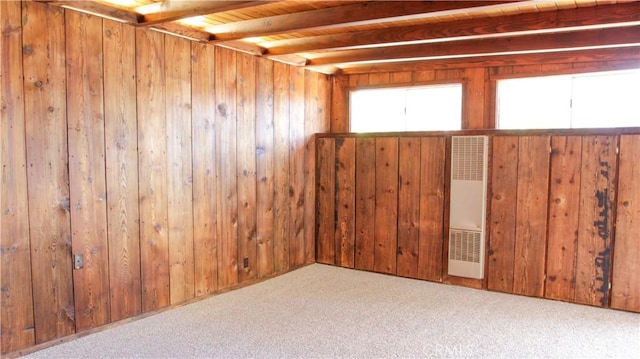 carpeted empty room featuring wood walls, a heating unit, and beamed ceiling