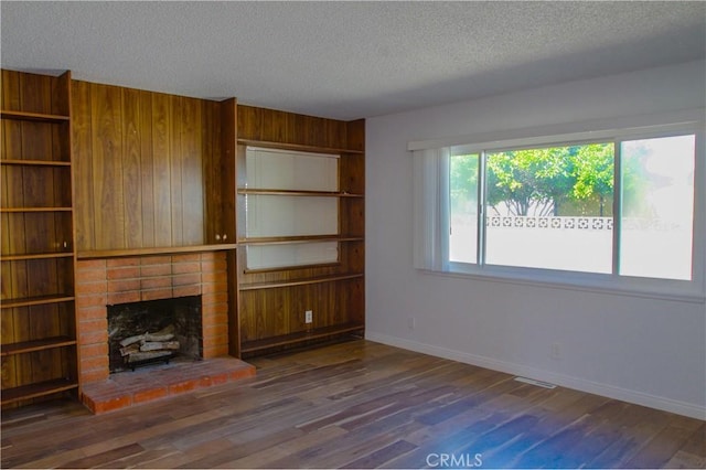 unfurnished living room with a textured ceiling, a fireplace, wood finished floors, baseboards, and wooden walls
