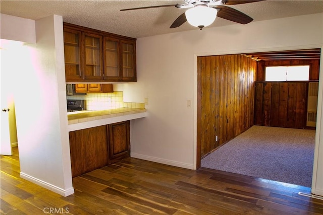kitchen featuring dark wood-style flooring, a ceiling fan, backsplash, glass insert cabinets, and baseboards