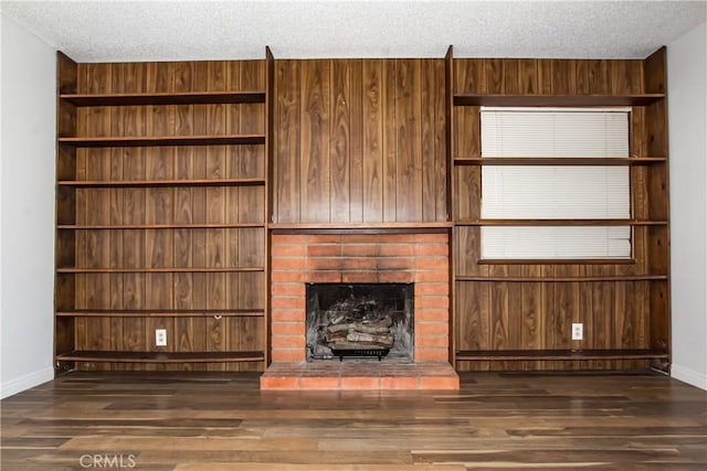 unfurnished living room with a textured ceiling, wood finished floors, baseboards, a brick fireplace, and wooden walls