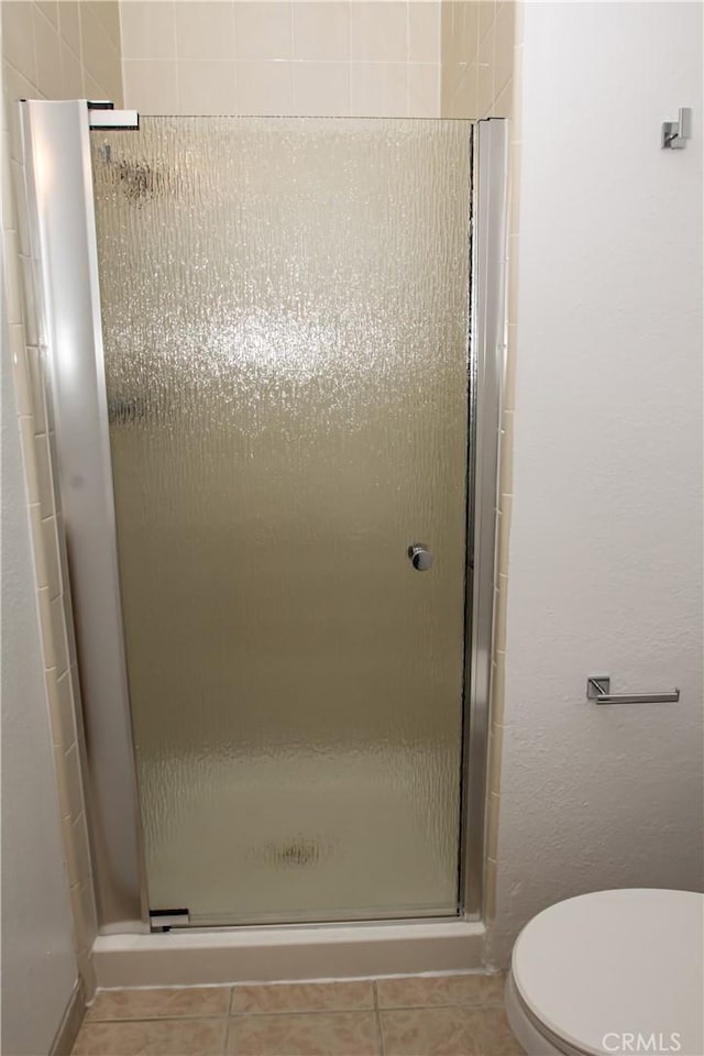 bathroom featuring a shower stall, tile patterned flooring, and toilet