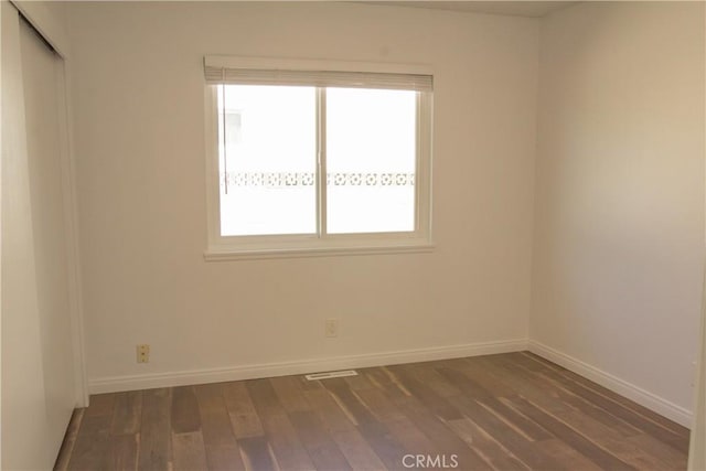 unfurnished room with plenty of natural light, dark wood finished floors, and baseboards