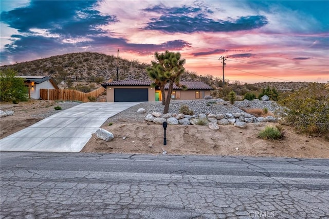 8244 Balsa Ave, Yucca Valley, CA 92284 - view of front facade with concrete driveway, a tile roof, a garage, a mountain view, and stucco siding